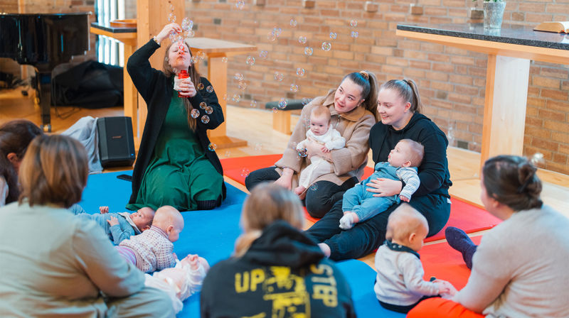 Kateketen Bente synger, forteller, blåser såpebobler og spiller av musikk fra en liten bærbar høyttaler. Foto: Den norske kirke