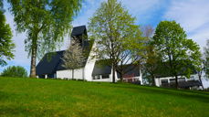 Holmen kirke i frodig grønt landskap. Fotograf: Norunn Edvardsen