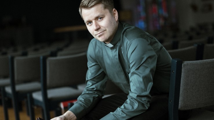 En diakon som sitter fremoverlent på en stol. 