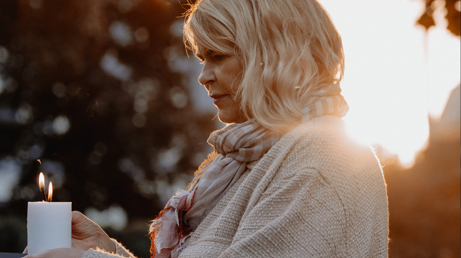 Kvinne tenner lys. Hun står ute og holder lyset i hendene.