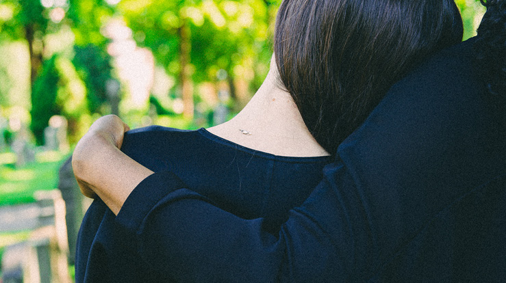 En person legger hodet mot skulderen til en annen. De er kledd i sorte klær. De er i begravelse.