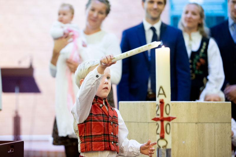 Et barn tenner et lys. Han må strekke seg opp for å rekke det. Dåpsfamilien står rett bak.