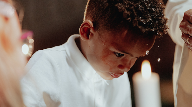 En liten gutt bøyer seg over døpefonten og lar seg døpe.