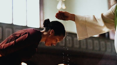 En kvinne lener seg over døpefonten og lar seg døpe.