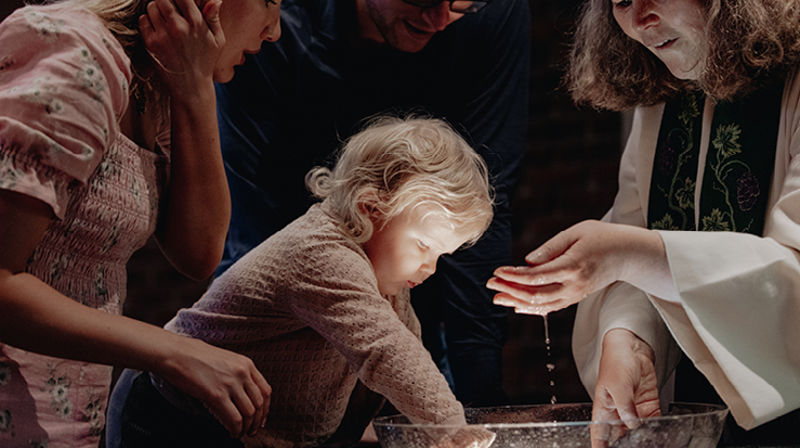 Et parn krabber på døpefonten og kikker interessert i vannet. Hun skal bli døpt.