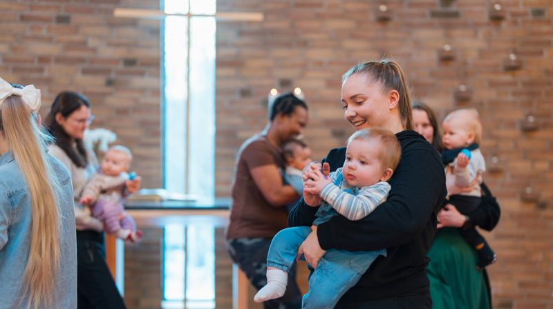 Flere mødre som bærer sine små barn på babysang i kirken, de går i sirkel og smiler