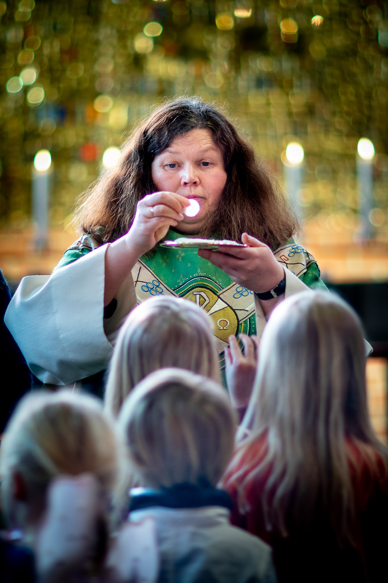 En prest holder opp en oblat, brødet i nattverden, mens en kø har gjort seg klar for å ta imot og spise, under nattverdsutdelingen i gudstjenesten.