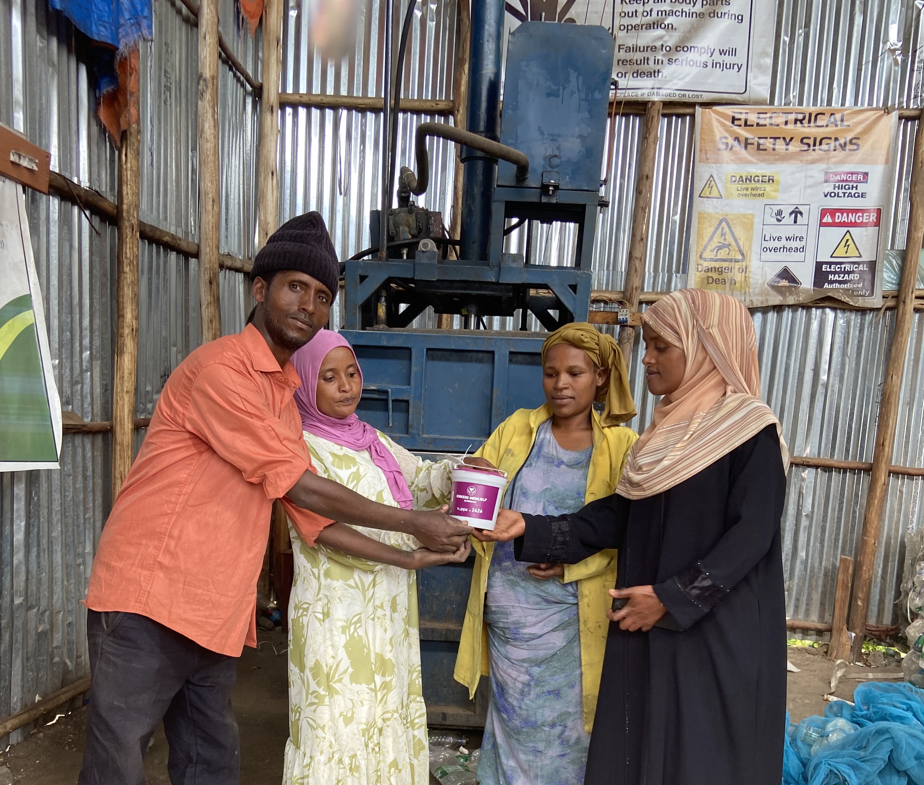 PRESSE: Her står Jemilla Senbete (nr 2 f.v.)  med venner foran pressen som de har fått støtte  av Kirkens Nødhjelp til å skaffe. De presser  plastflaskene sammen, som siden blir remser det  flettes kurver av.