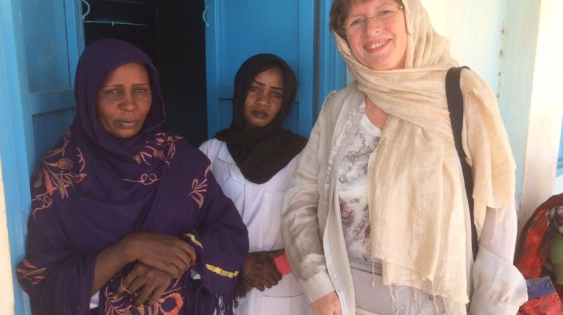 Ingeborg i Darfur utenfor en fødestue, sammen med søster og mor til en fødende kvinne. De har båret med seg 8 jerrykanner med vann til fødselen fordi fødestuen ikke hadde innlagt vann