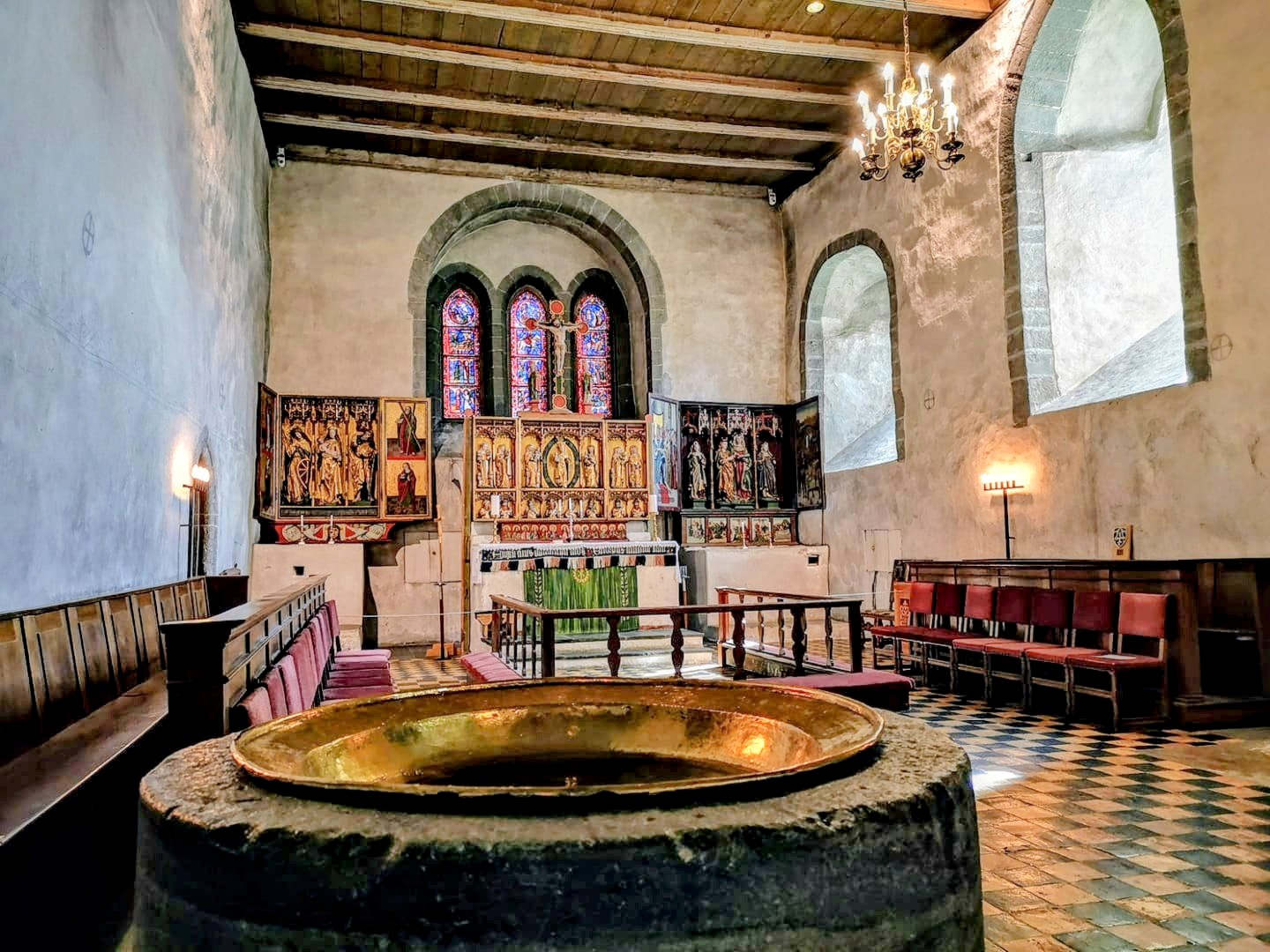 Trondenes kirke i Harstad var blant mottakerne av tilskudd i forrige runde. Her er kirkens altertavle, med romansk døpefont i forgrunnen. Foto: Den norske kirke.