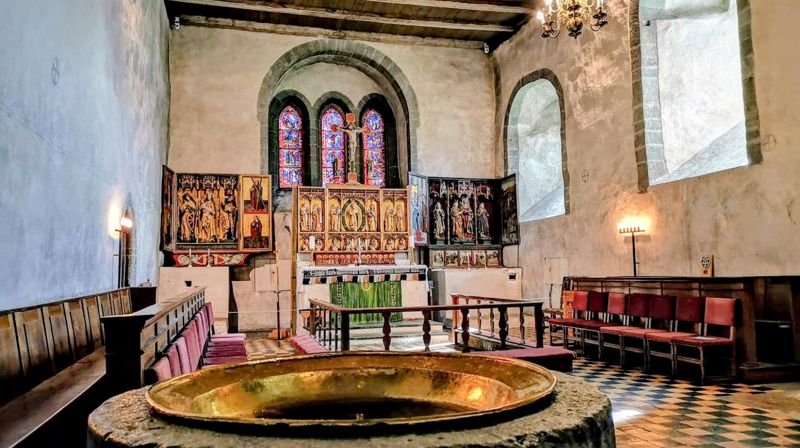Trondenes kirke i Harstad var blant mottakerne av tilskudd i forrige runde. Her er kirkens altertavle, med romansk døpefont i forgrunnen. Foto: Den norske kirke.