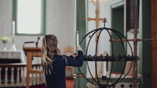 Jente plasserer et tent lys i lysgloben i Saltdal kirke. Foto: Frida Bringslimark