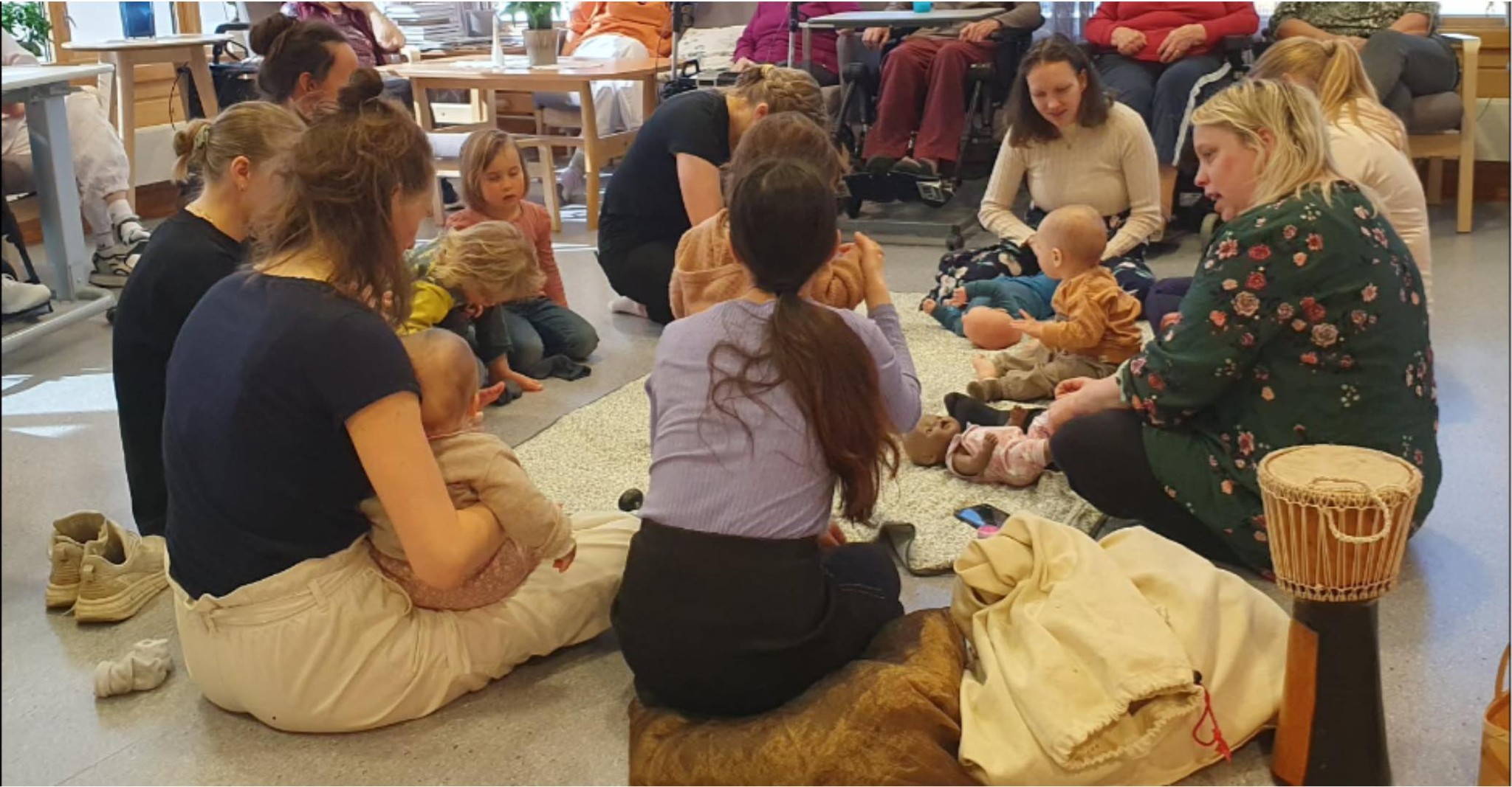 Vaksne med babyar sit i ring på golvet.