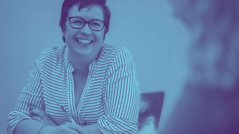 Kvinne i jobbsituasjon smiler. Blåtoner. Foto.