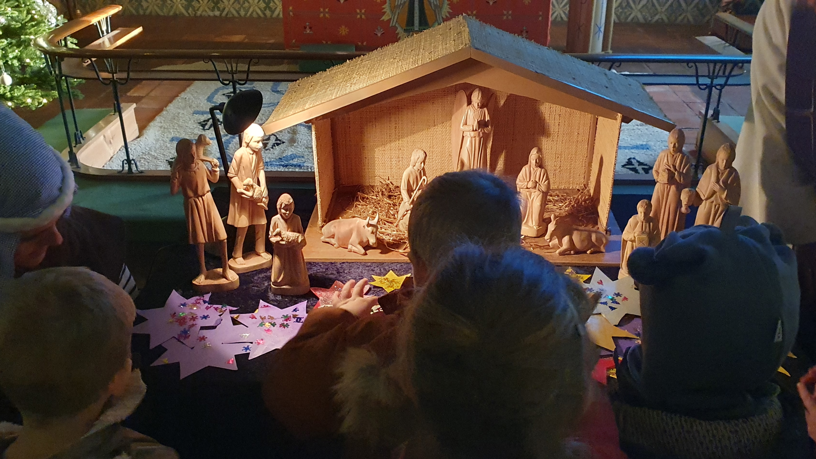 Barnehagebarn legger fra seg sine fint dekorerte stjerner foran julekrybba i Bakkebø kirke.