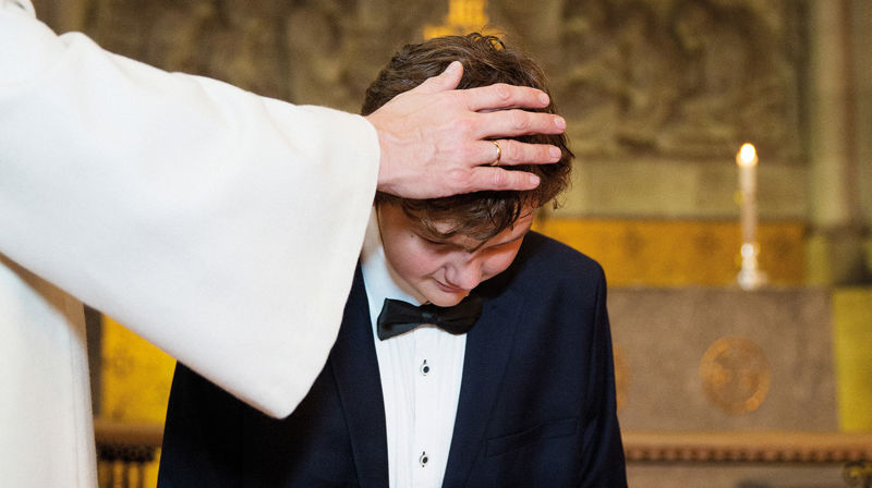 En ung gutt blir døpt. Presten har hånden på hodet hans. Han blir nå medlem i kirken.