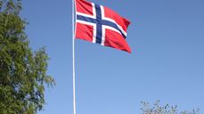 Det norske flagget vaier i vinden omkranset av bjørk og morell i vårblomstring. Foto: Kirken i Gran, Inger S. Haug.