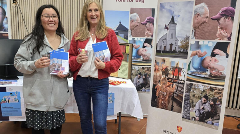 To damer står på stand og siler, de holder oppe brosjyrer de skal dele ut