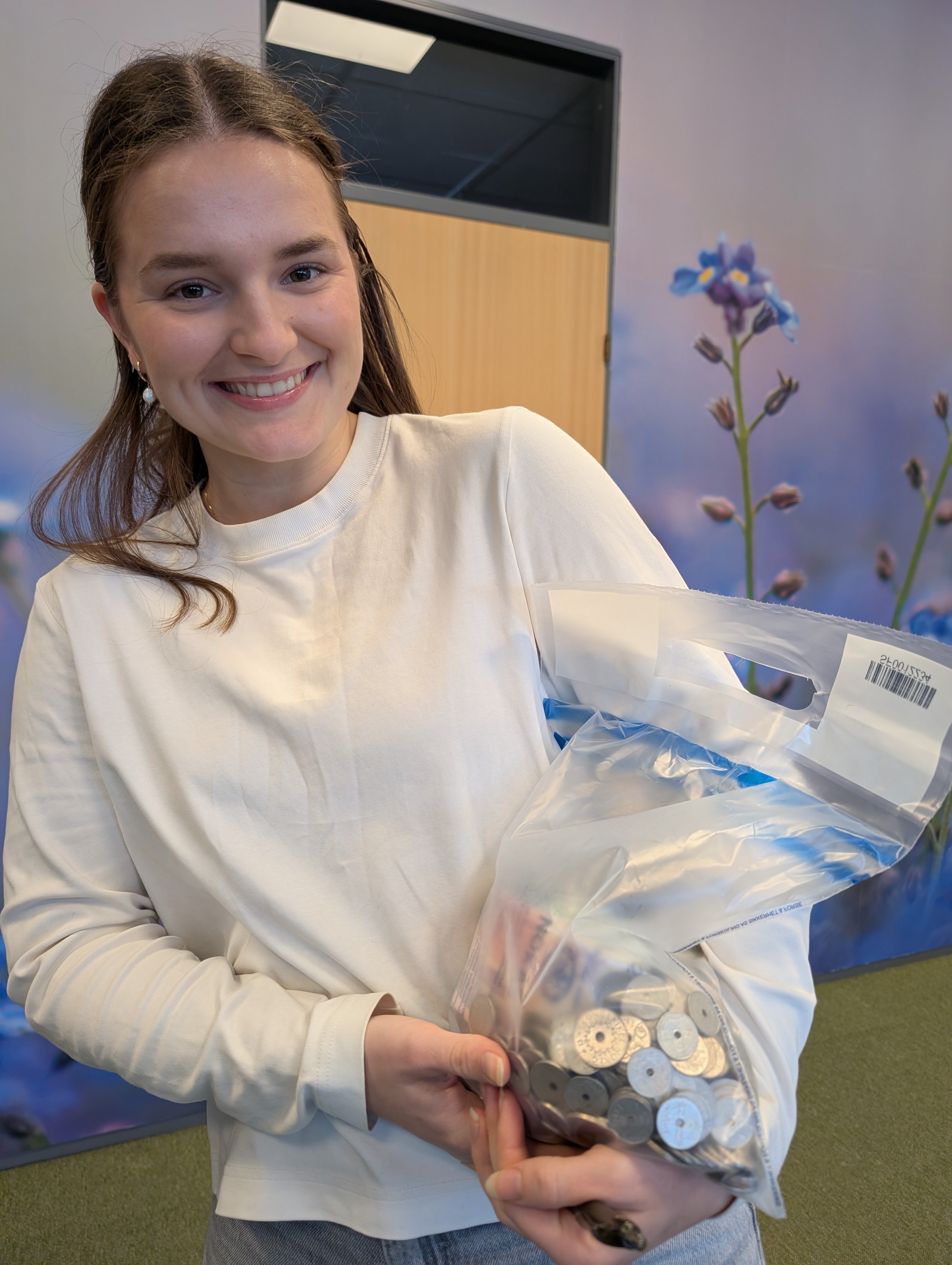 En dame holder smilende opp en gjennomsiktig pose med mange mynter oppi