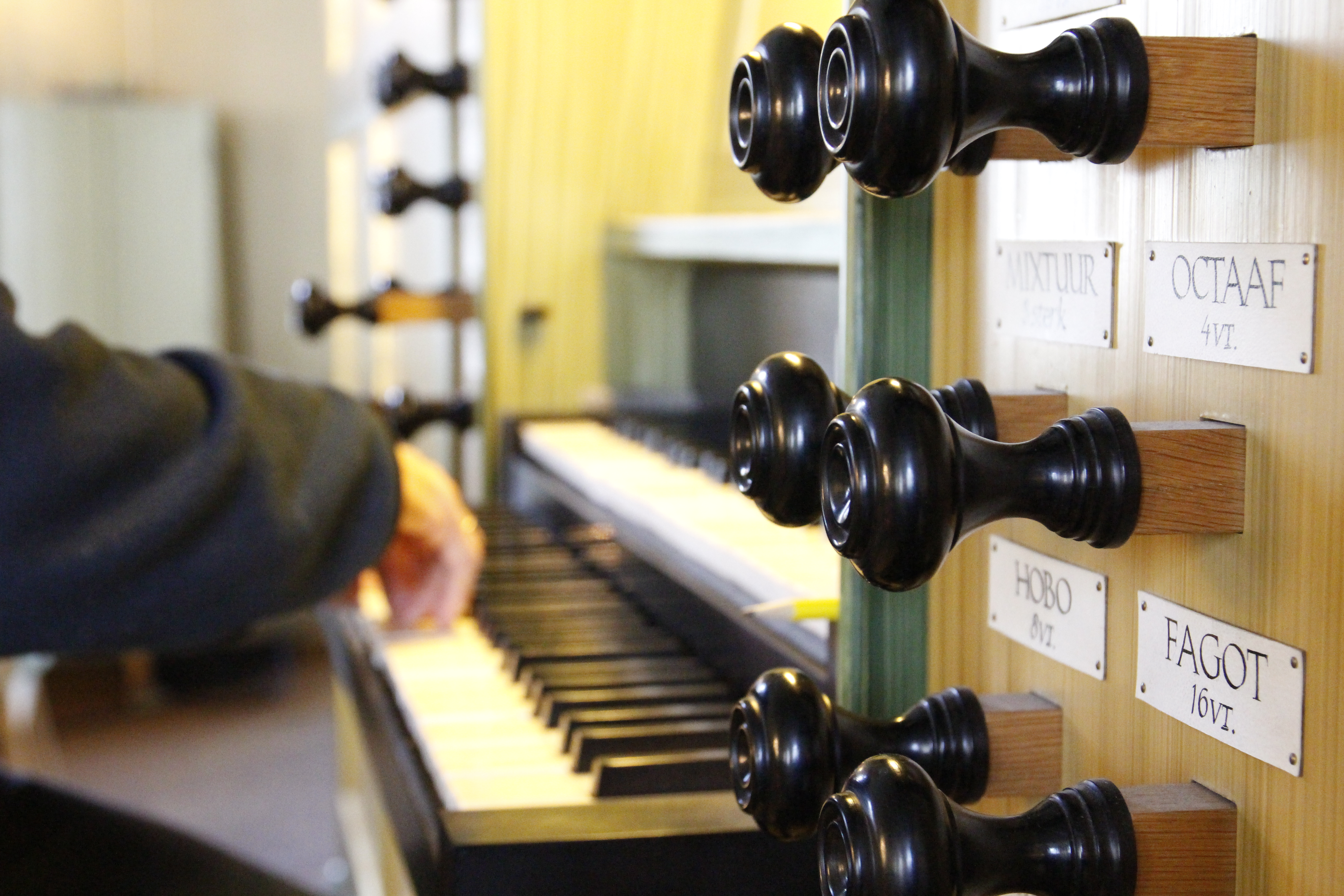 Nærbilde av registerknappene på et orgel i Fjell kyrkje, man kan se hender spille på tangentene i bakgrunne