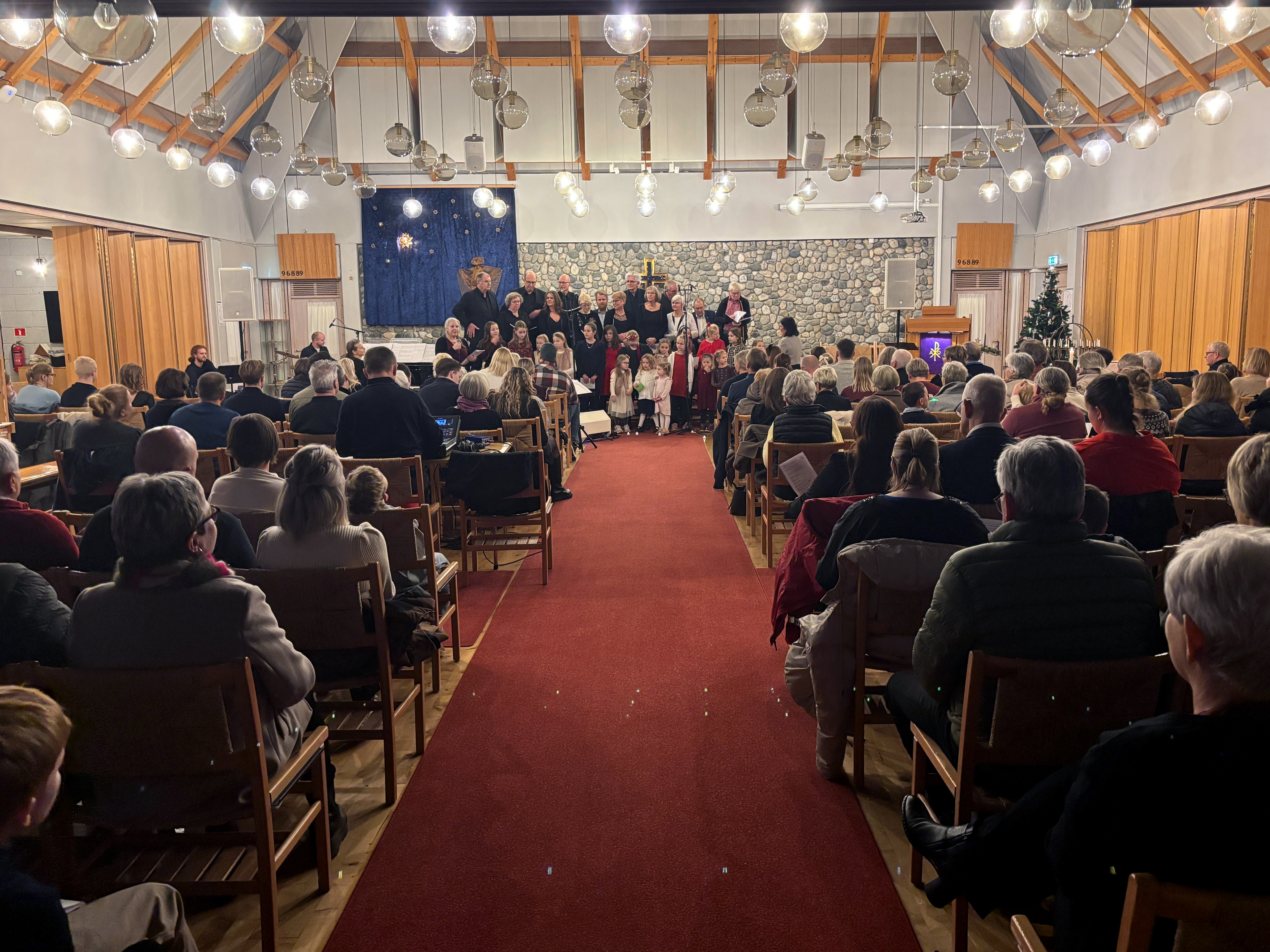 To kor, et barnekor, og et voksenkor, st&aring;r fremme i kirken. Stolene i kirkeskipet er full av menneske