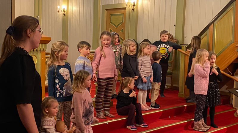 Barn står og sitter i trappen fremme i kirken, de ser mot der dirigenten står