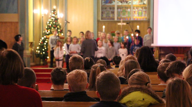 Skulebarn sitt i benkradene i kyrkja, dei ser på nokon som fremfører noko under skulegudsteneste