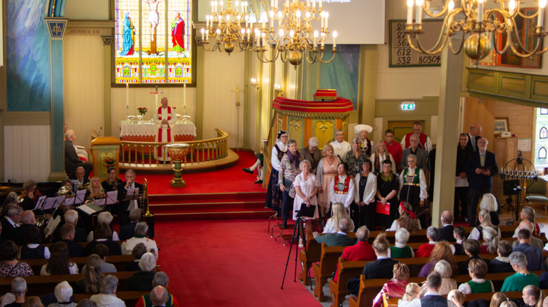 Oversiktsbilde fra galleriet, presten står oppe ved alteret, jubileumskoret under preikestolen, kyrkjebrassen til venstre. Fulle benker.