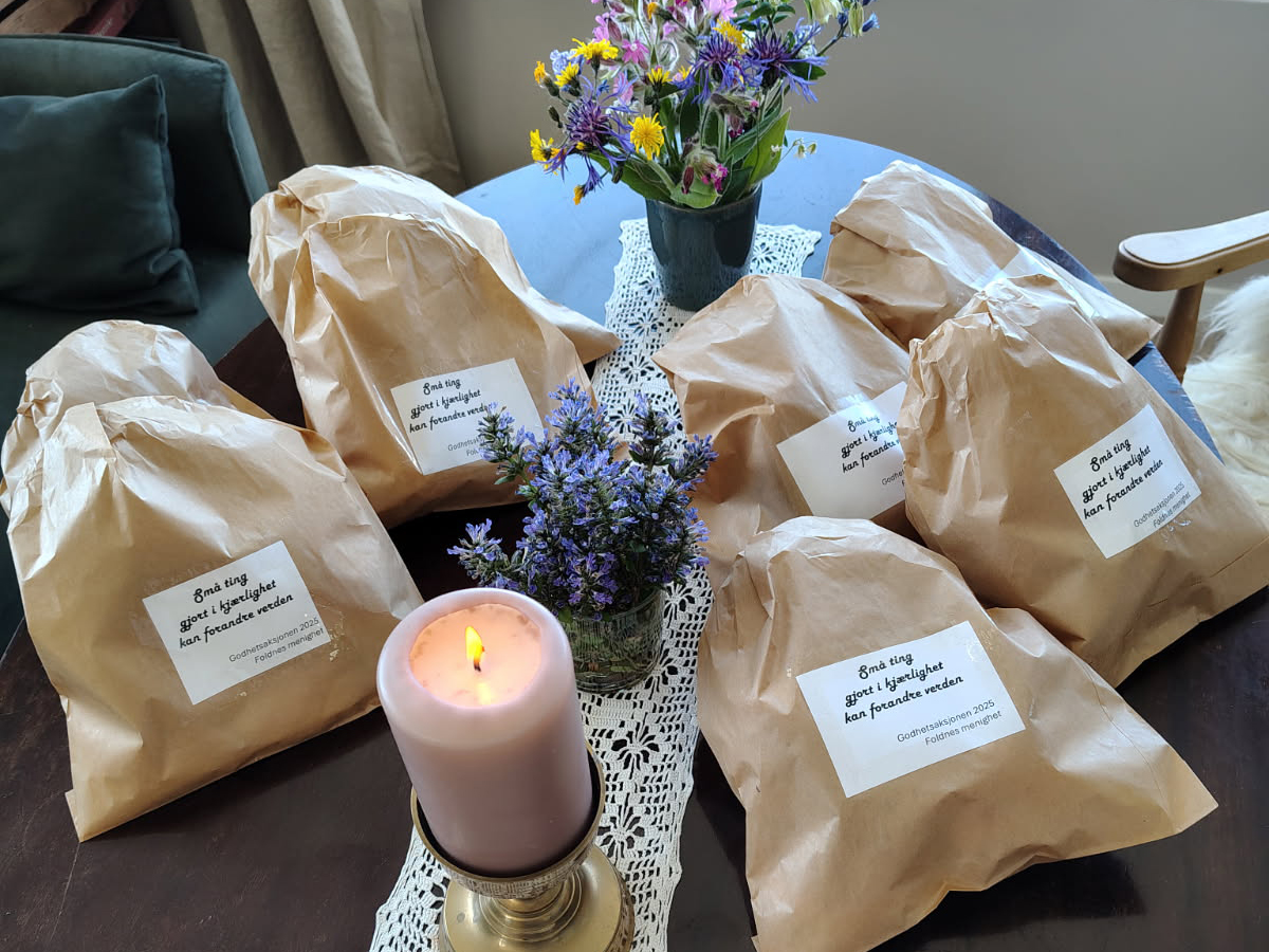 Et bord med brune papirposer, et lys og to enkle blomsterbuketter. En hilsen på en hvit lapp utenpå posene: "Små ting gjort i kjærleik kan forandre verda. 