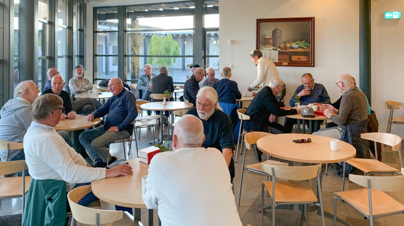 Menn sitter rundt flere småbord og prater sammen