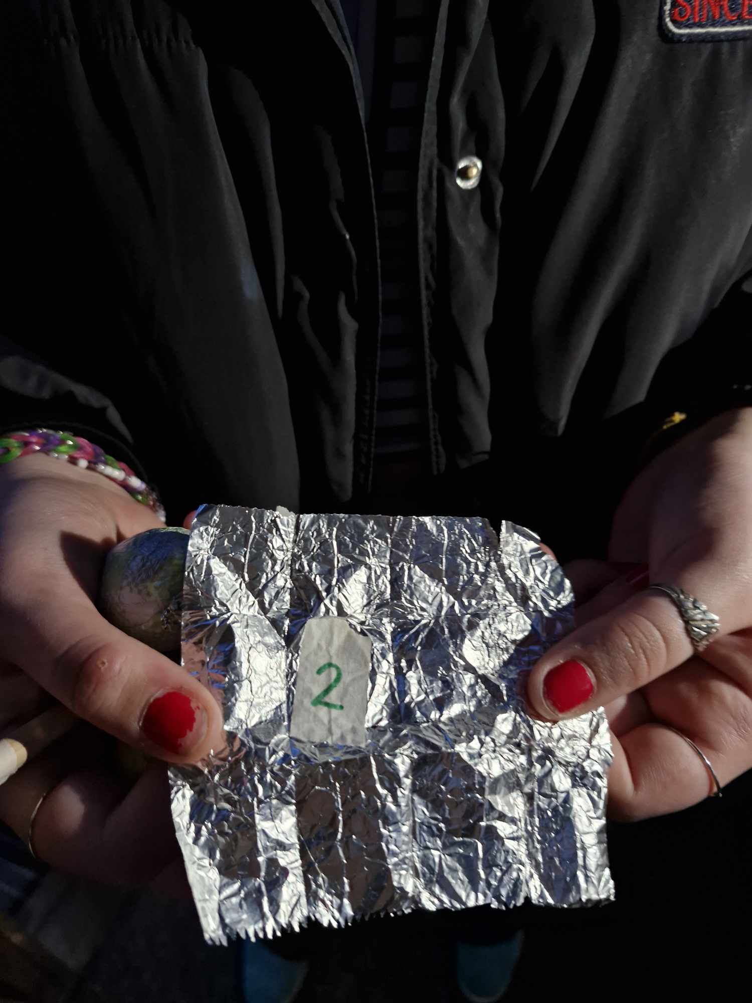 Eit par hender held eit stykke aluminiumsfolie med talet 2 på.