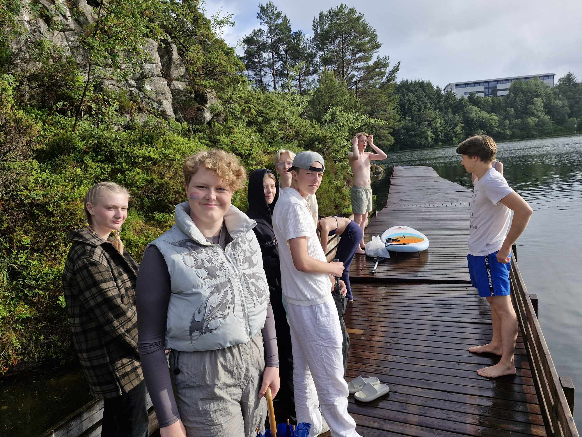 Ungdommar står på brygga, nokon i vanlege klede og nokon er klar for å bade