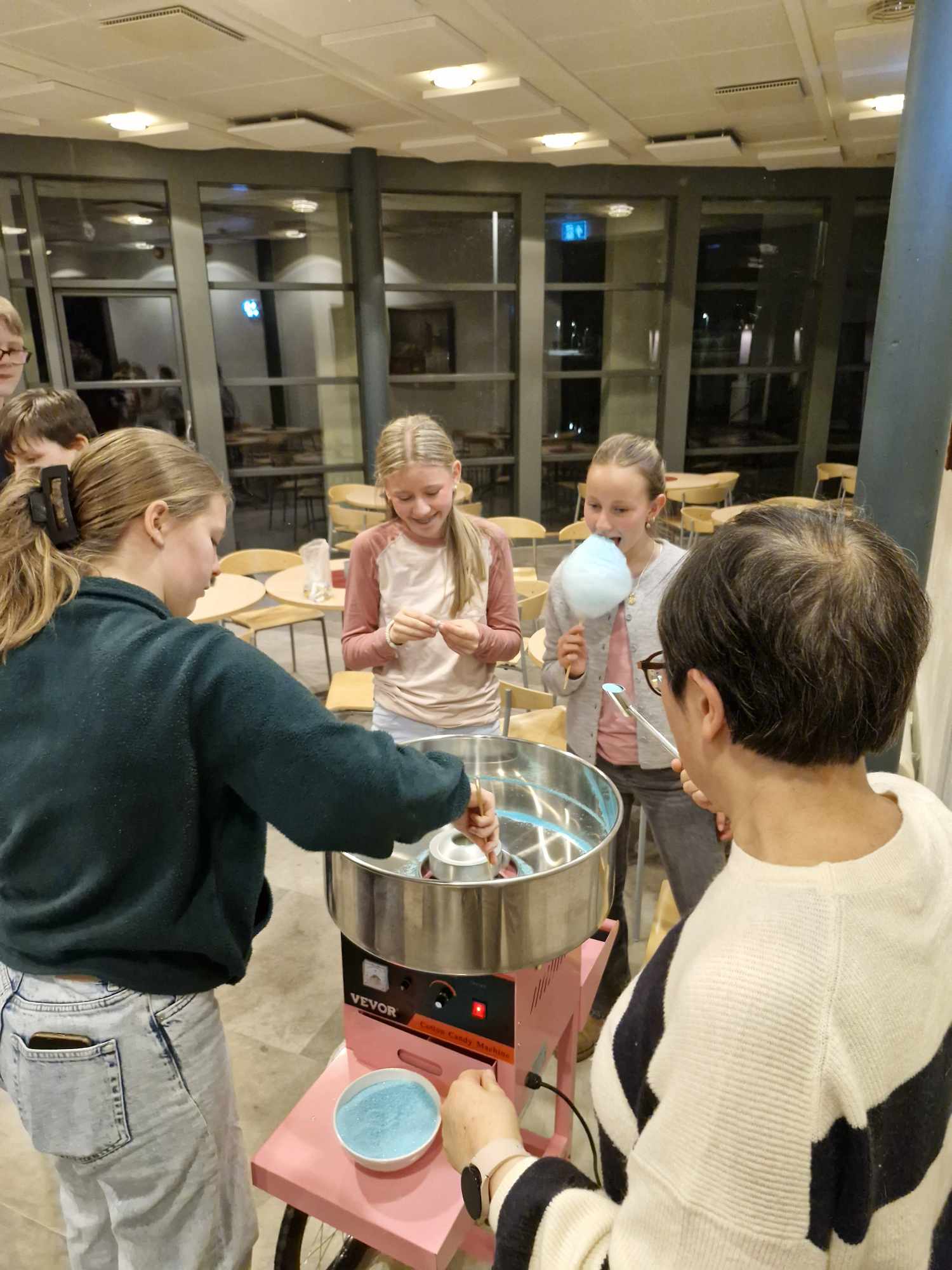 Ungdommar står rundt ei sukkerspinnmaskin og lager og et blått sukkerspinn