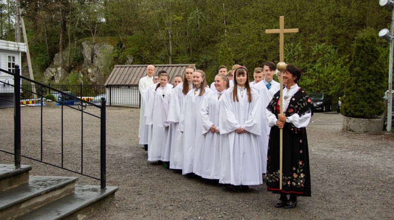 Konfirmantar med kvit kappe som står oppstilt utanfor Fjell kyrkje.