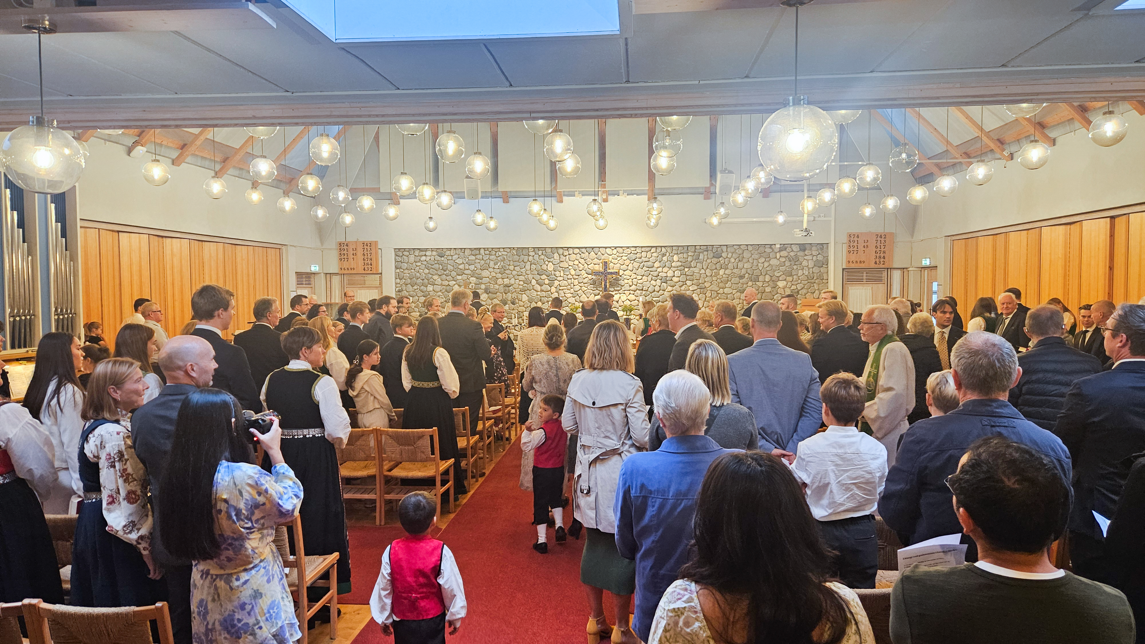 mennesker står i stolradene og ser på inngangsprosesjonen til gudstenesten