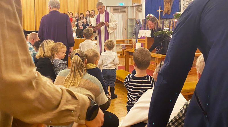 Prest og pedagog står framme i kyrkja og deler ut bøker til tre-åringer som er med foreldre og besteforeldre