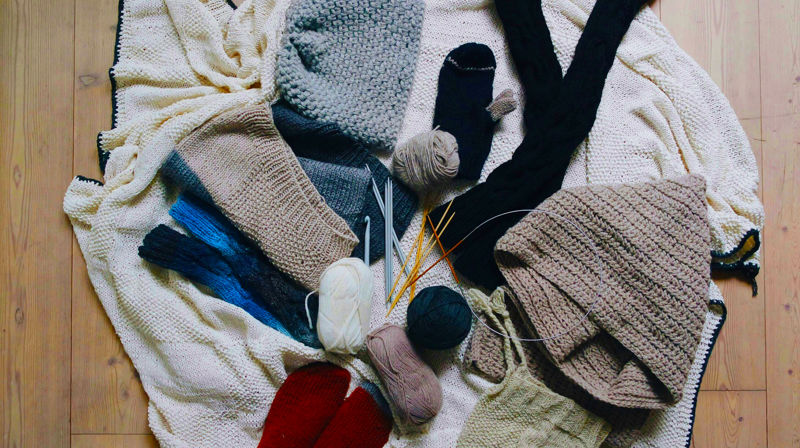 Strikketøy, garn og strikkepinner ligger utover et gulv