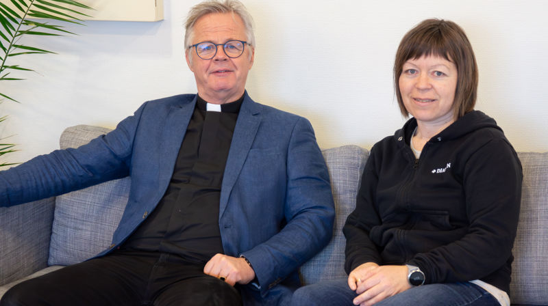 En prest og en diakon sitter på en sofa og ser inn i kameraet