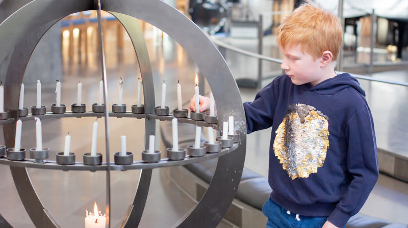 En gutt står ved lysgloben i Foldnes kyrkje og tenner et lys