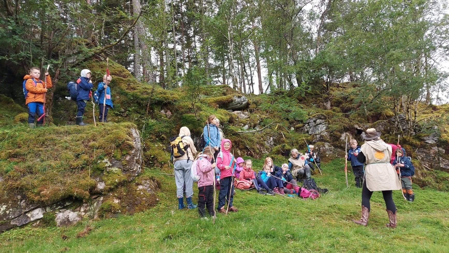 Åtteåringar står ute i naturen og er på tur , dei har pilegrimsstavar  og ser på ei leiar som snakkar