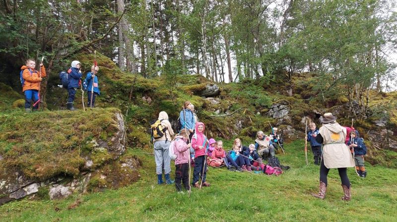Åtteåringar står ute i naturen og er på tur , dei har pilegrimsstavar  og ser på ei leiar som snakkar