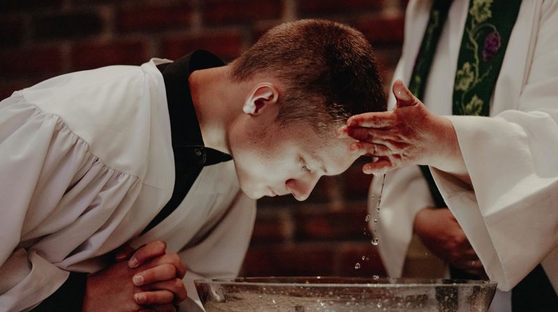 Ung mann døpes i hvit kappe i DNK.  Foto Malin