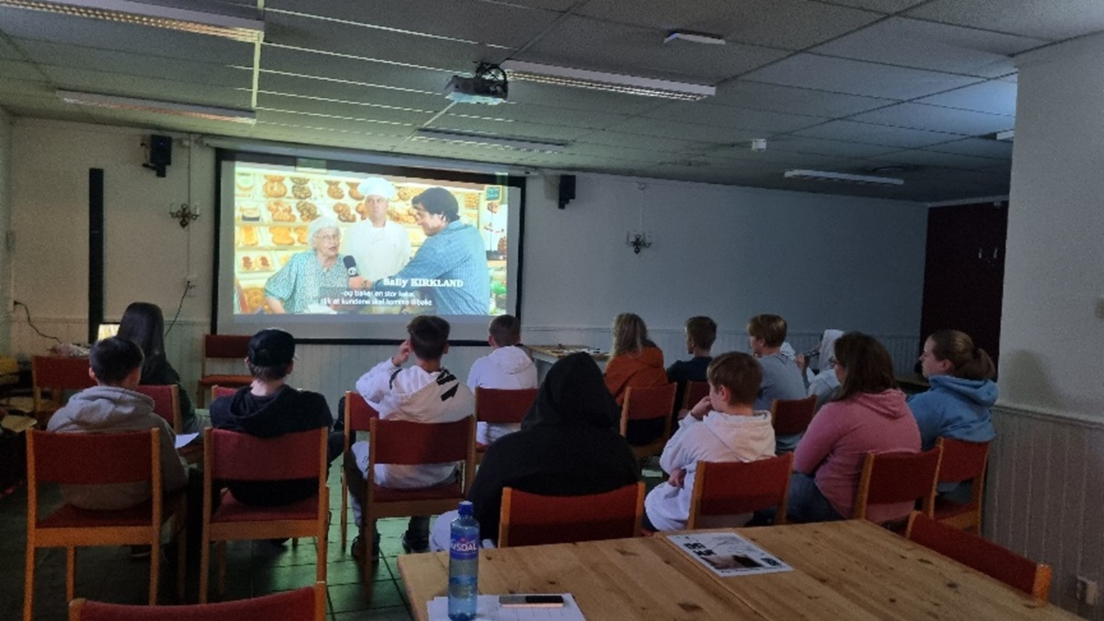 Mange konfirmanter sitter og  ser på en film på storskjerm