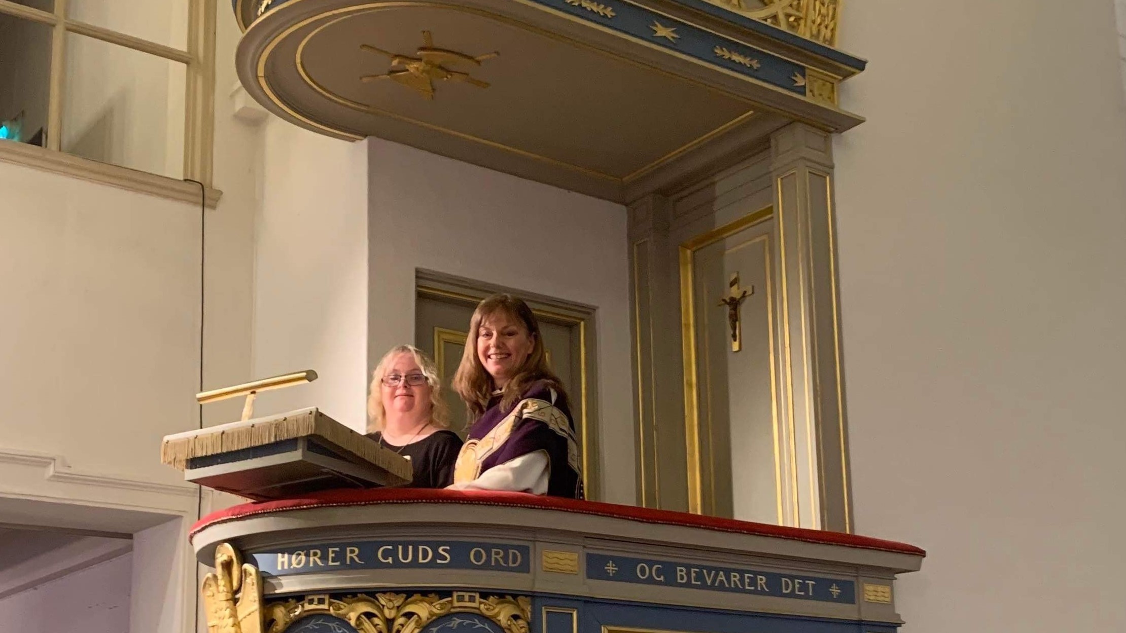 Hanne Arnstad og Hege Fagermoen som står sammen på prekestolen og smiler til kirkerommet.