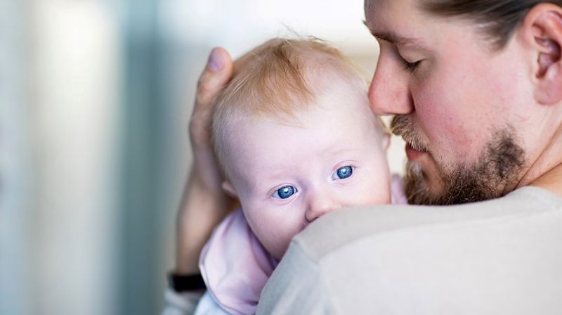 En baby holdes tett inntil brystet av en mann