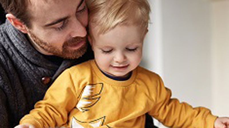 En voksen mann som sitter med et barn på fanget, og leser en bok.